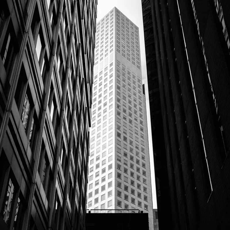 A monochrome architectural photograph looking upward between modern city buildings